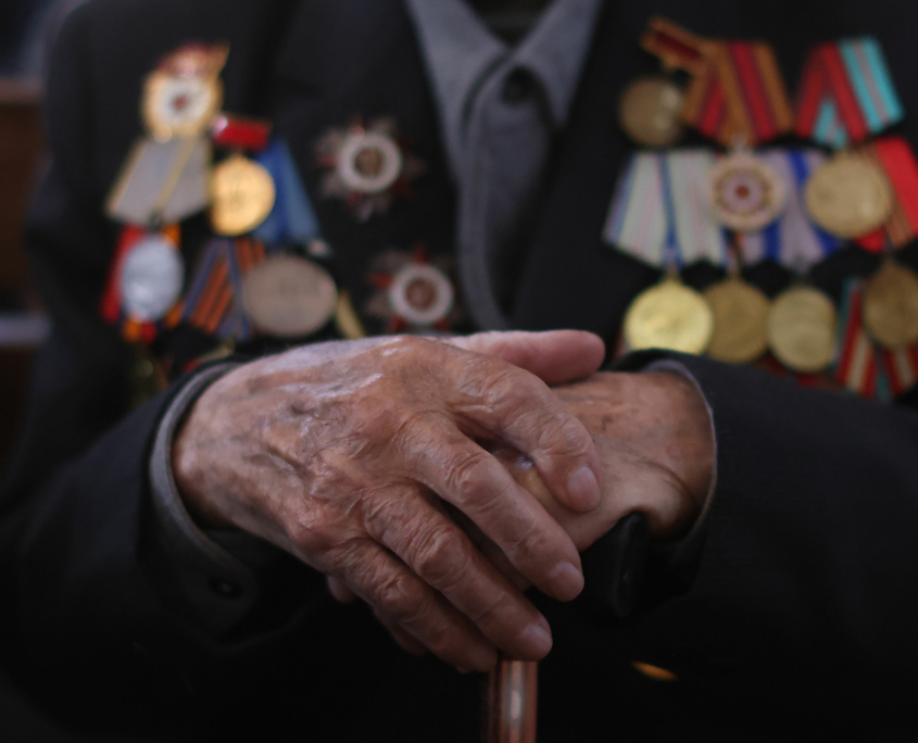 Closeup of the hands of an elderly war veteran with a lot of medals
