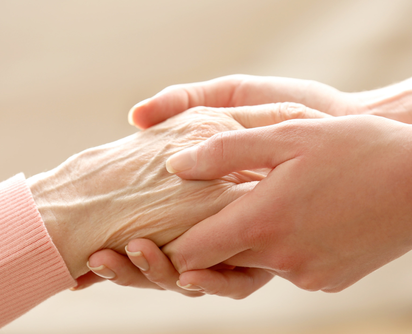 Side view of a caretaker holding an elderly woman's hand