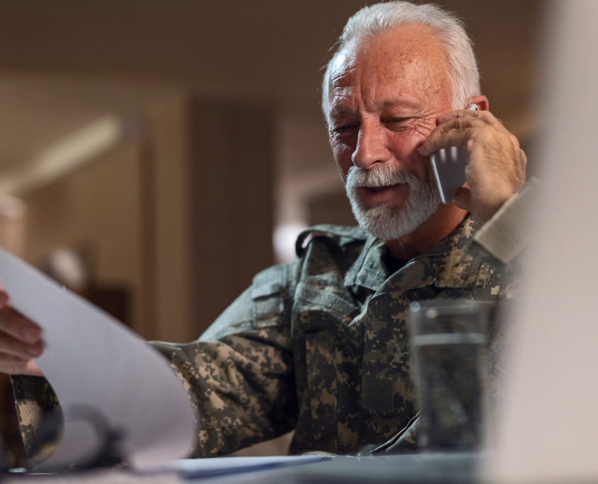 Side view of an elderly veteran reading paper documents while talking on the phone